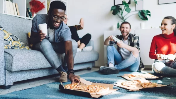 Four friends enjoying each other's company while eating pizza in a living area and laughing