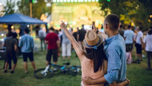 A couple taking a video of the small, outdoor concert happening in front of them